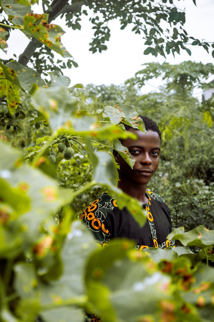 Portrait of a young man wearing traditional attire surrounded by vibrant green foliage.